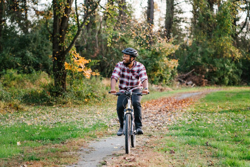 Man wearing flannel on a mountain bike rides on a flat, stone trail in a state park amid scattered leaves in fall.