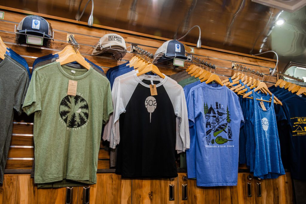 A rack displaying a variety of Delaware State Park t-shirts and hats in different colors and styles.